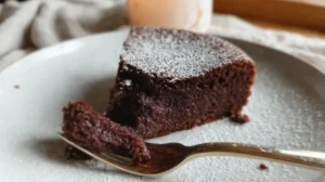 Part de moelleux au chocolat sur assiette blanche, texture fondante, fine couche de sucre glace sur le dessus.