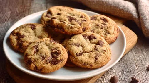 Cookies maison aux pépites de chocolat sur une assiette blanche en bois, texture moelleuse visible.