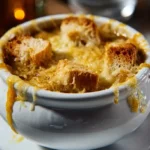 Soupe à l’oignon gratinée au fromage doré dans un bol en céramique, servie bien chaude.